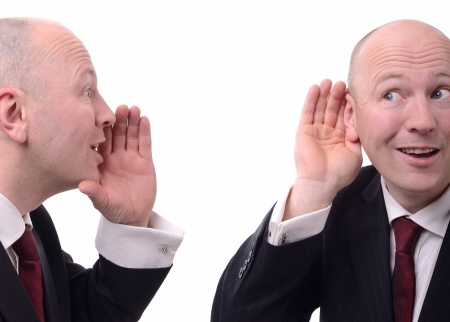 Man with his hand cupping his ear as another identical man cups his mouth saying something to him