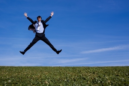 Man in a business suit jumping in the air with his hands up out in a field