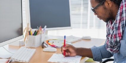 man drawing on a piece of paper at his desk