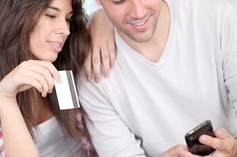 Man looking at his phone as a girl sits next to him holding a credit card