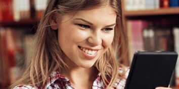 Woman smiling in a library scrolling on a tablet