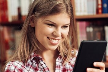 Woman smiling in a library scrolling on a tablet