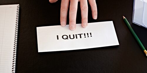 person pushing a piece of paper saying "I quit" on it