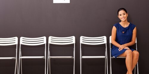 Woman sitting waiting to be interviewed with a row of empty chairs beside her