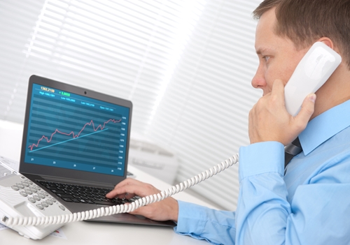 Man on a phone looking at a graph of his computer