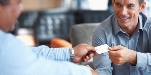 man giving his business card to another man while shaking his head